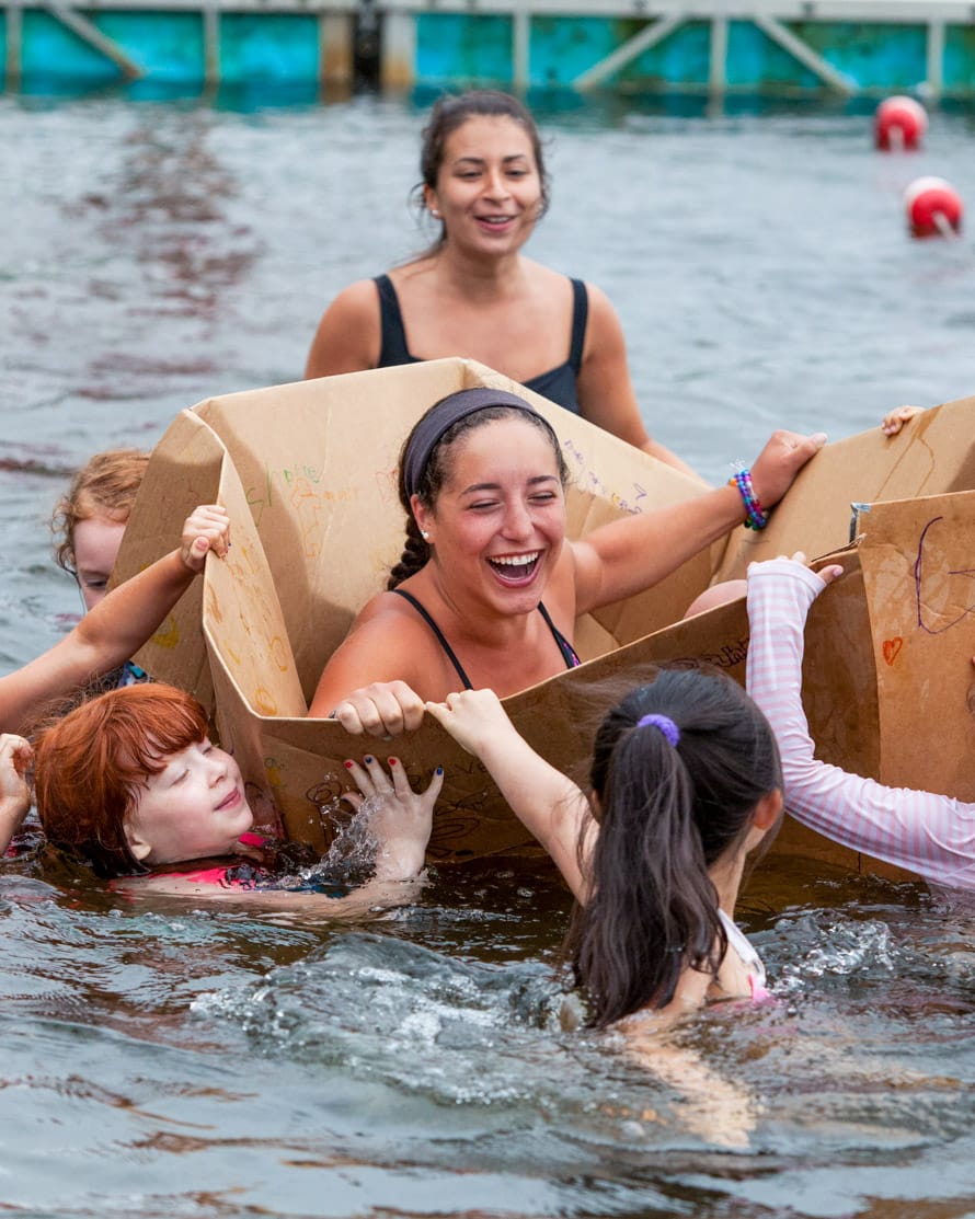 Camp staff in cardboard box in lake during special event